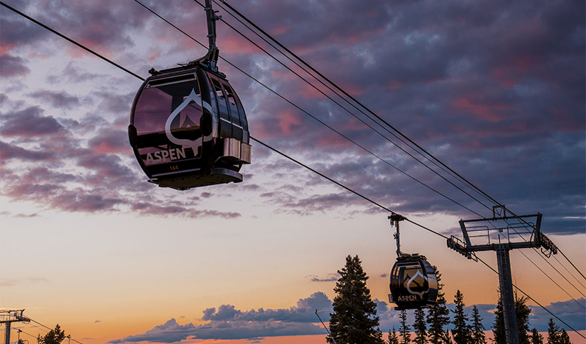 Silver Queen Gondola on Aspen Mountain at dusk, two gondola boxes are reflecting the sunset on their windows as they go up the mountain