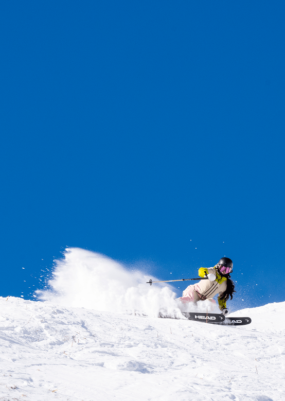skier carves into the snow on a blue bird day at Aspen, tossing snow towards the camera